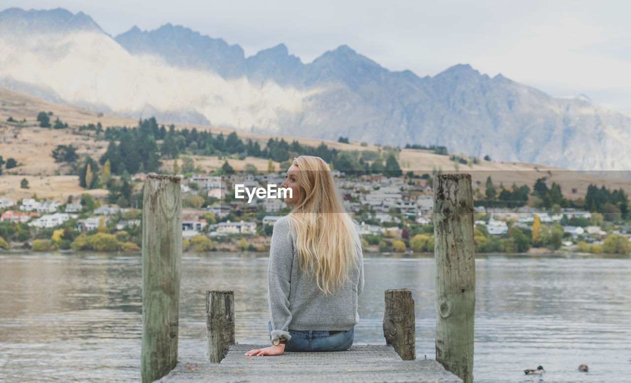 Rear view of young woman sitting on pier over lake