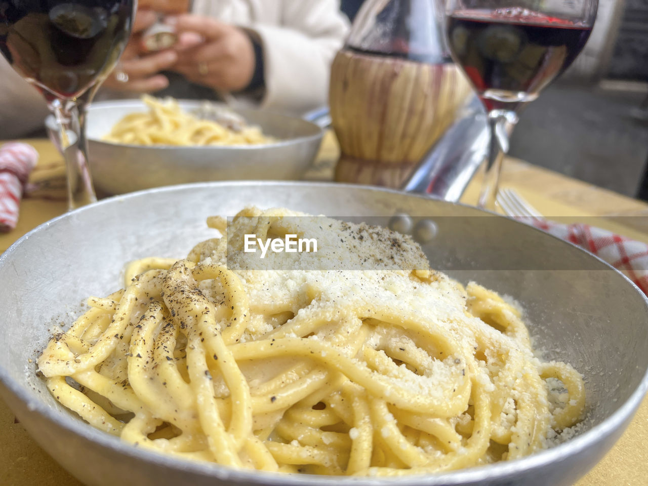 food and drink, food, pasta, pici, italian food, wine, wine glass, spaghetti, freshness, carbonara, household equipment, dish, cuisine, alcohol, glass, refreshment, drink, kitchen utensil, indoors, table, close-up, meal, red wine, business, plate, focus on foreground, one person, crockery, restaurant, drinking glass, dinner, domestic room, cheese