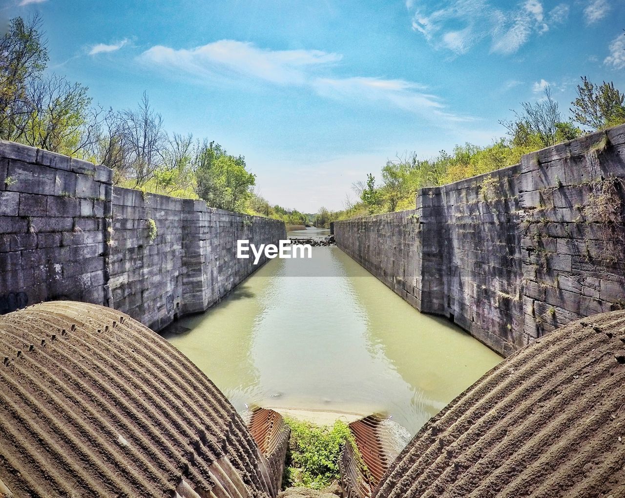 Scenic view of canal amidst wall during sunny day