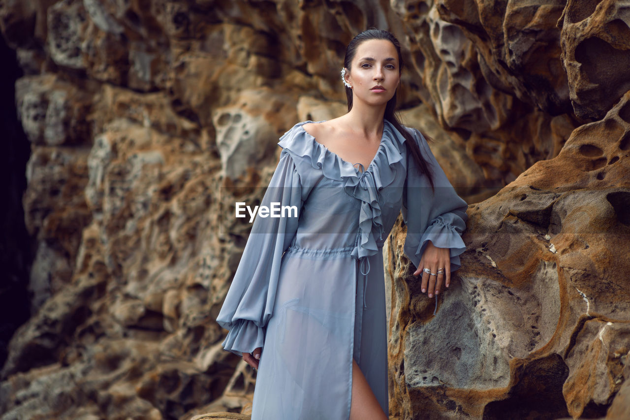 Fashionable brunette woman in a gray dress stands on a cheese rock in the summer