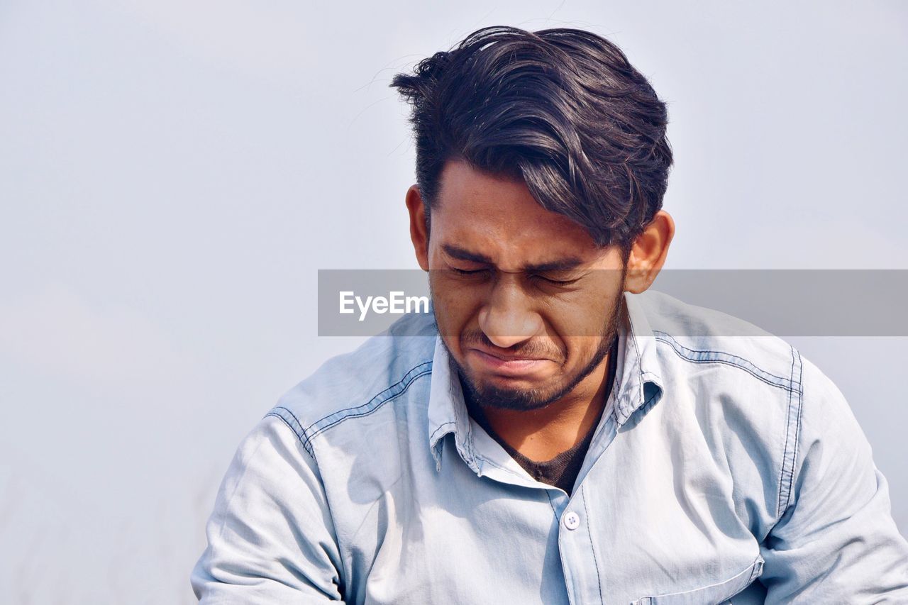 Sad young man with eyes closed against white background