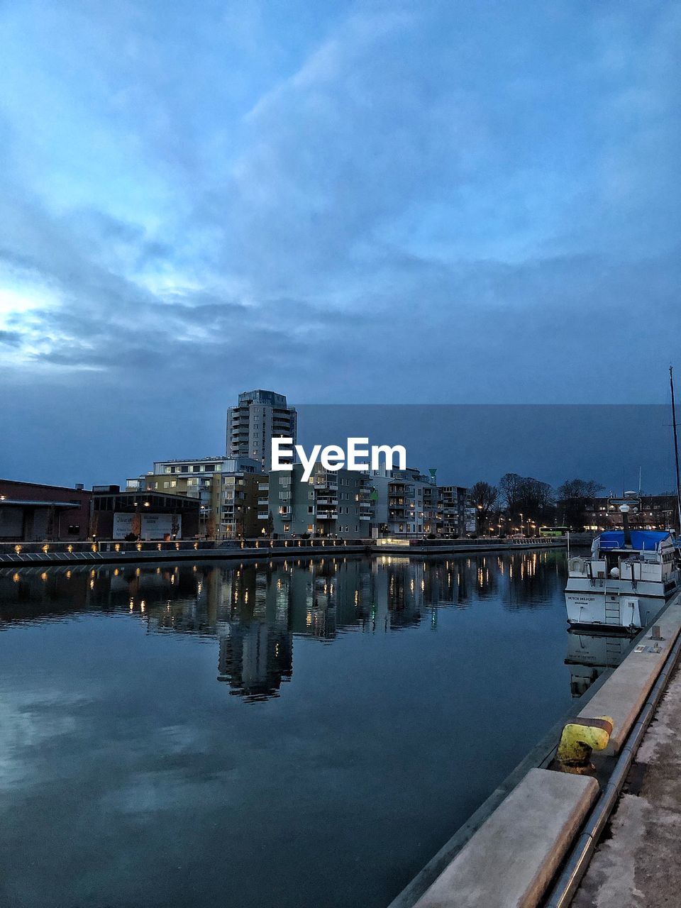 River by illuminated buildings against sky at dusk