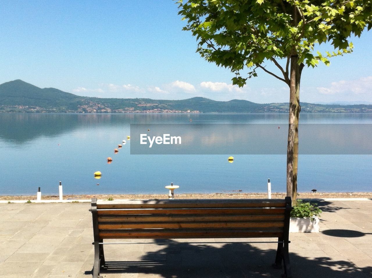 Empty bench by lake against sky