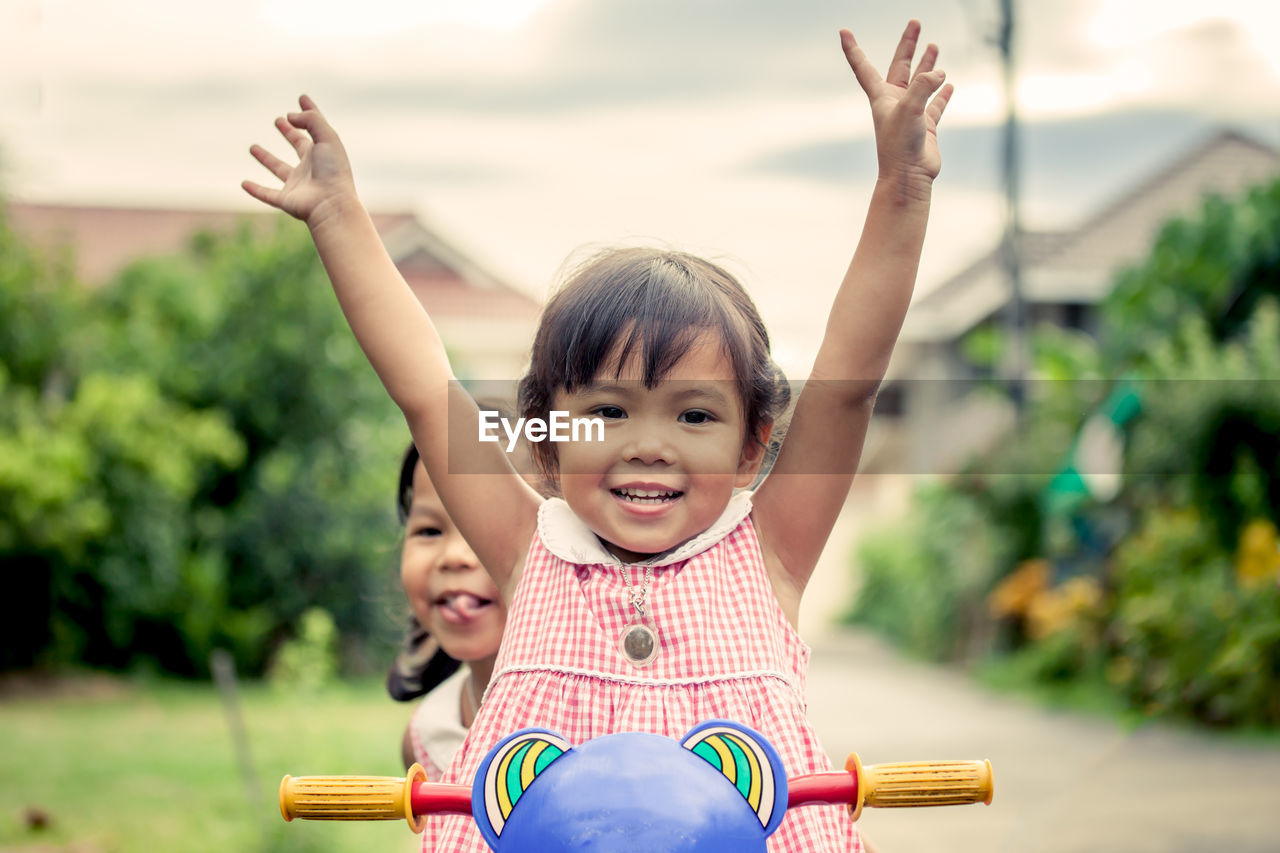 Sisters riding tricycle on road at public park