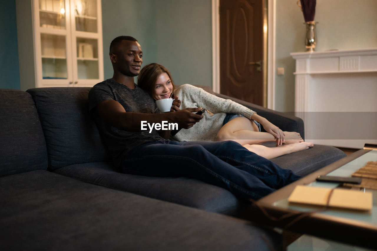 Diverse couple cuddling on sofa and watching tv together