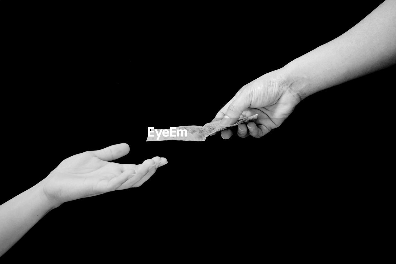 Close-up of hand giving money to friend over black background