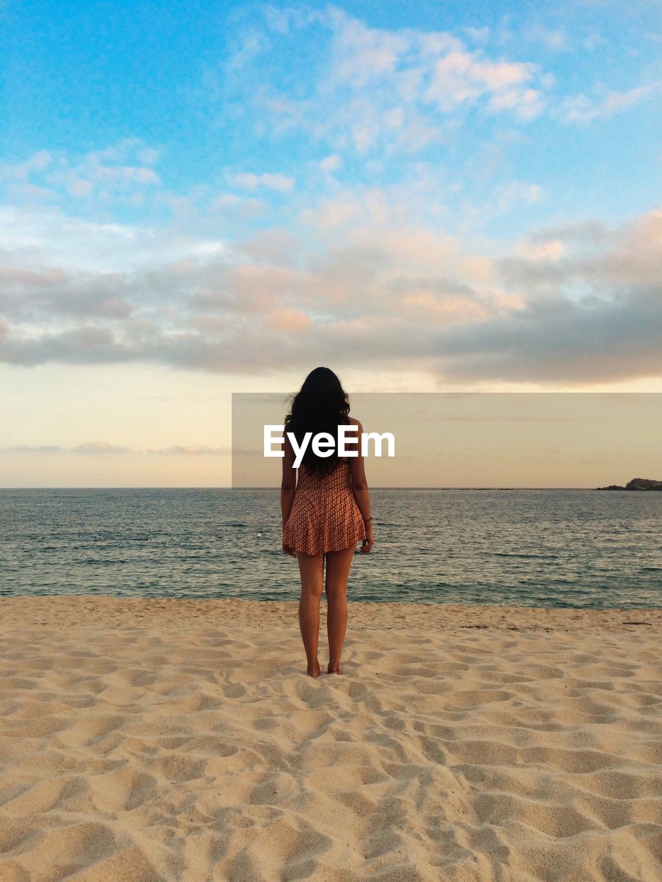 Rear view of woman standing on sand at beach against sky