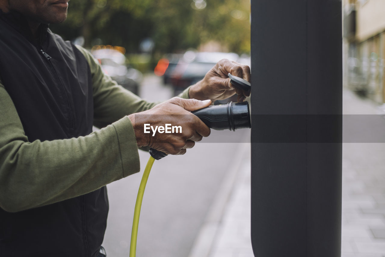 Man removing charger plug from kiosk at car charging station