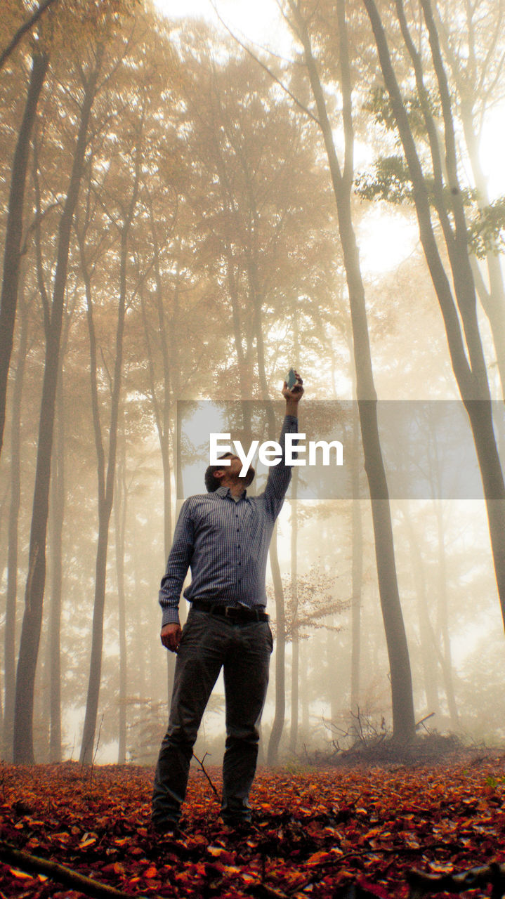 Full length of man standing with arms raised in forest during autumn