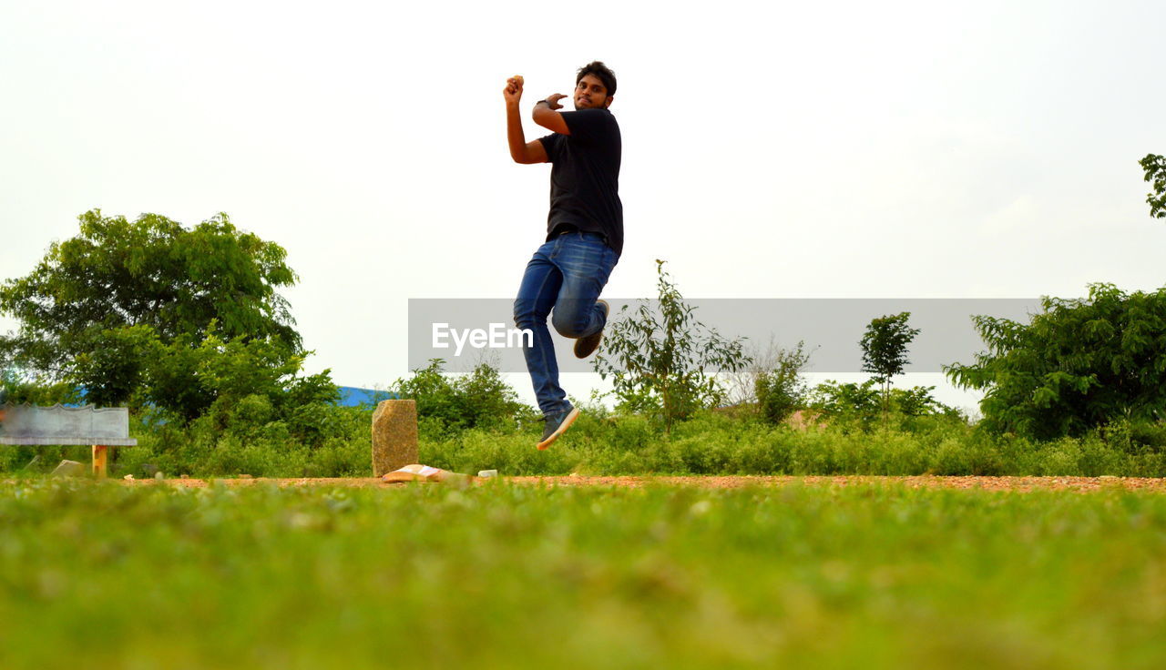 Man playing cricket on grassy field against clear sky