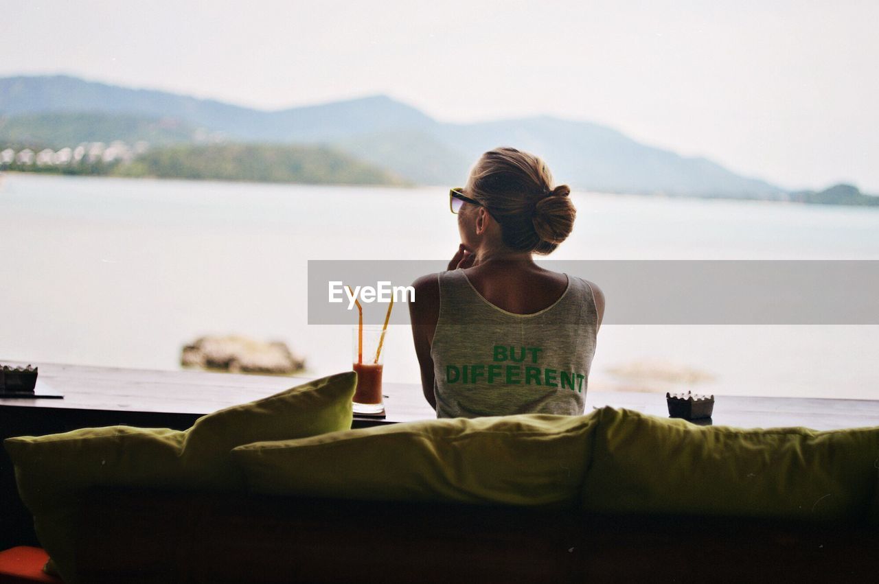 REAR VIEW OF WOMAN SITTING IN FRONT OF LAKE