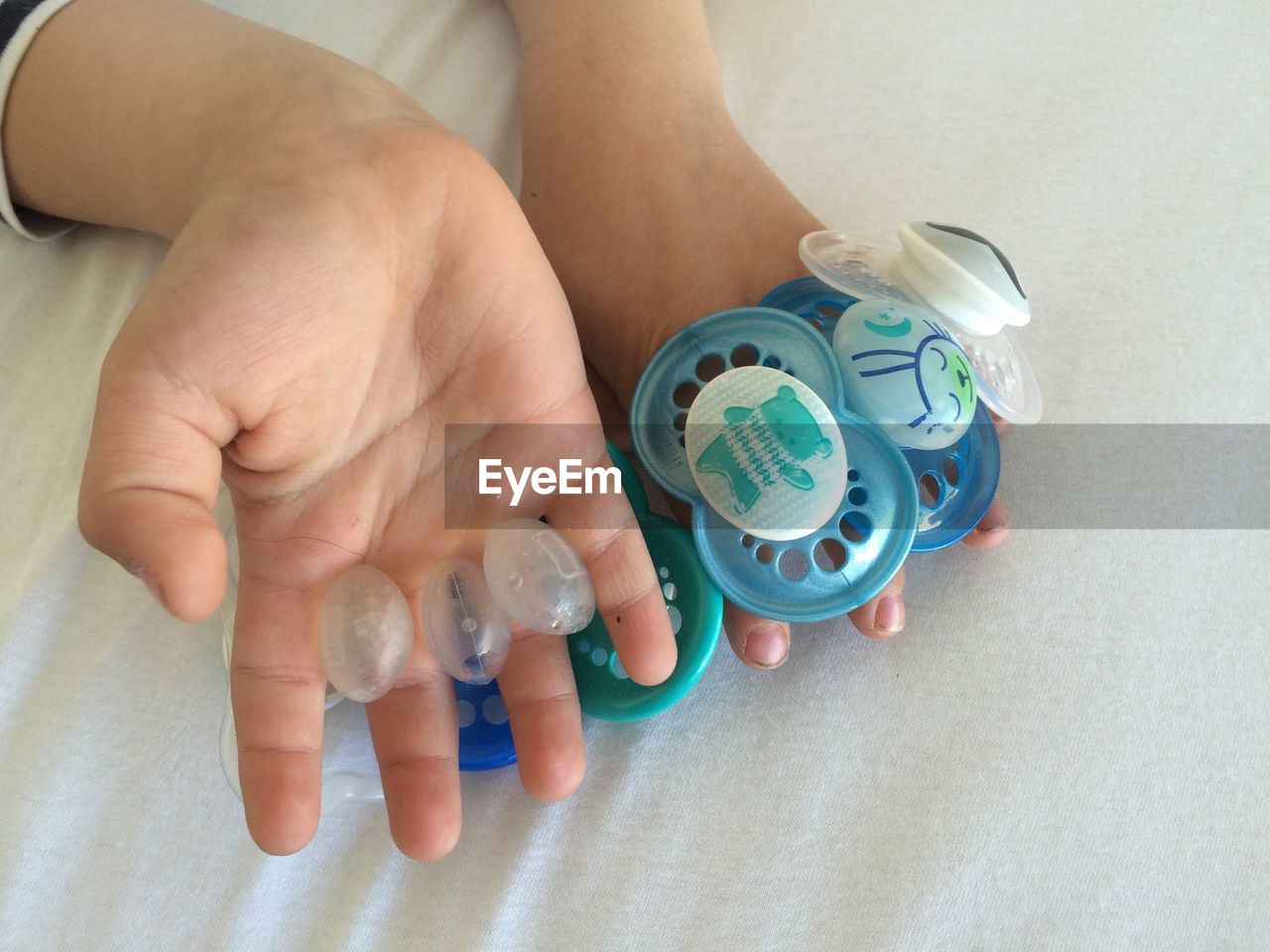 Cropped hands holding pacifiers on bed