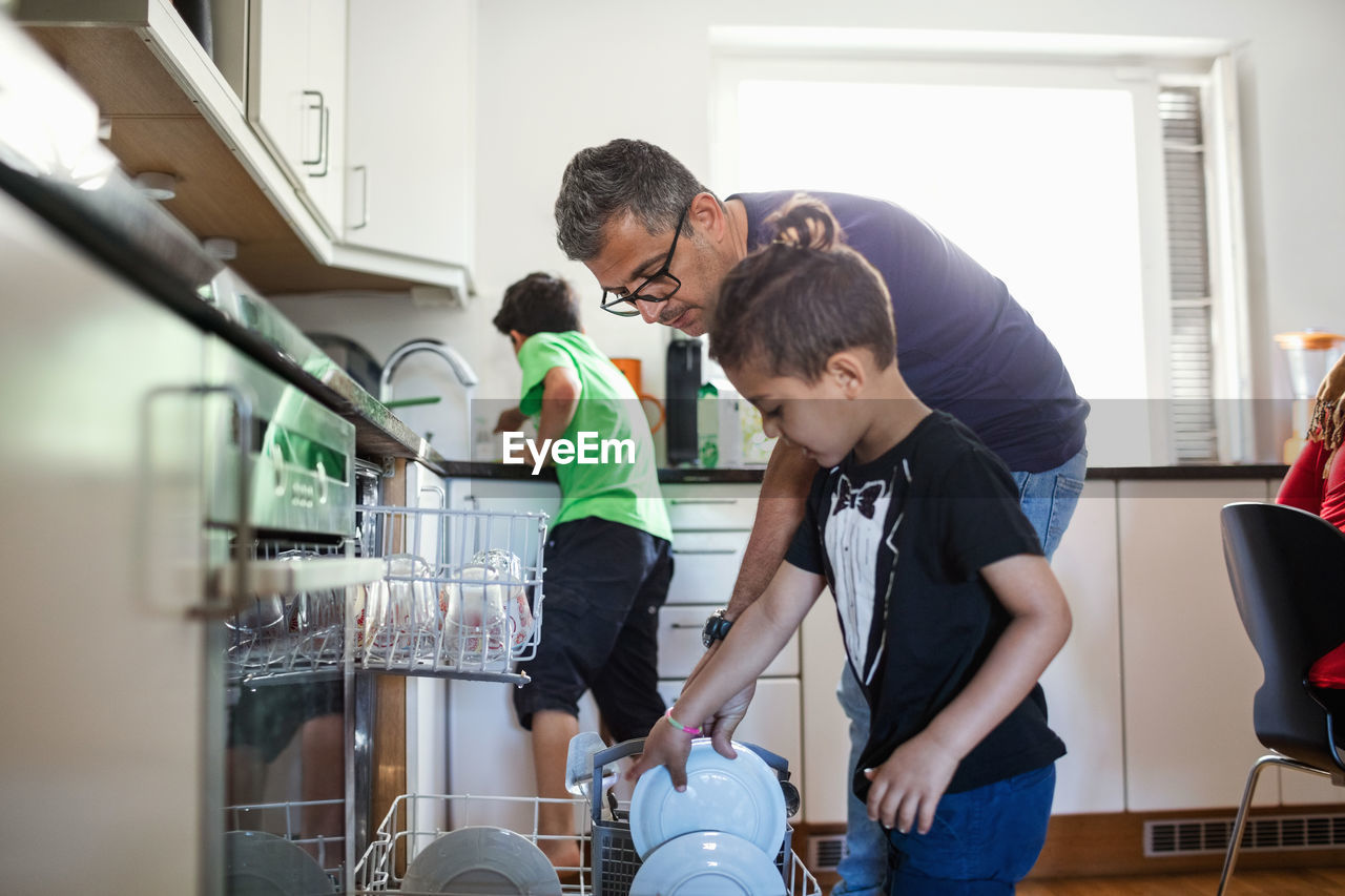 Father and son arranging plates in dishwasher at kitchen