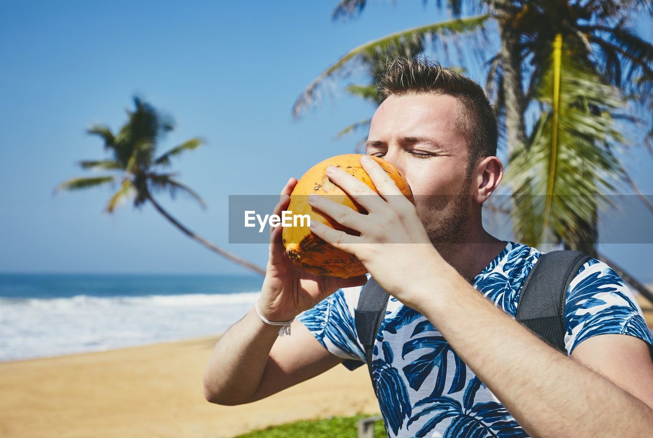Man drinking coconut at beach against sky