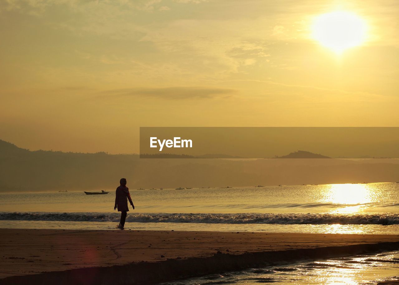 Woman walking on shore against sea during sunset