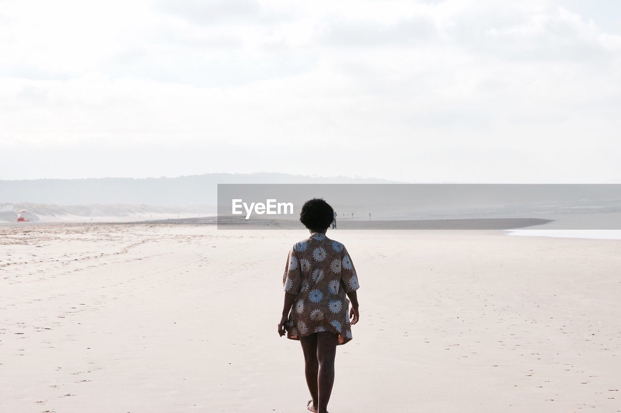 Rear view of woman walking on beach against sky