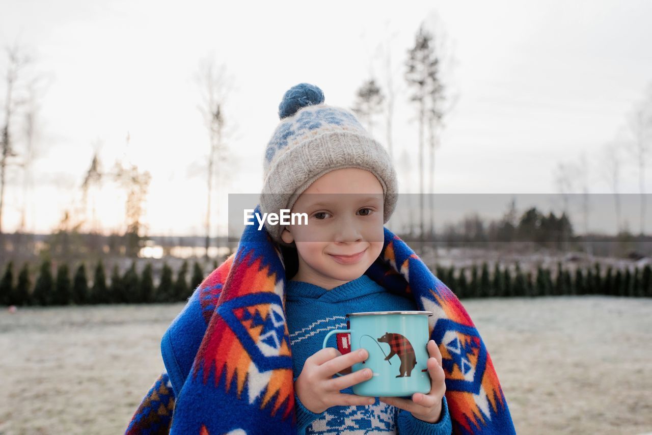Young boy smiling whilst wrapped in a blanket holding a hot chocolate