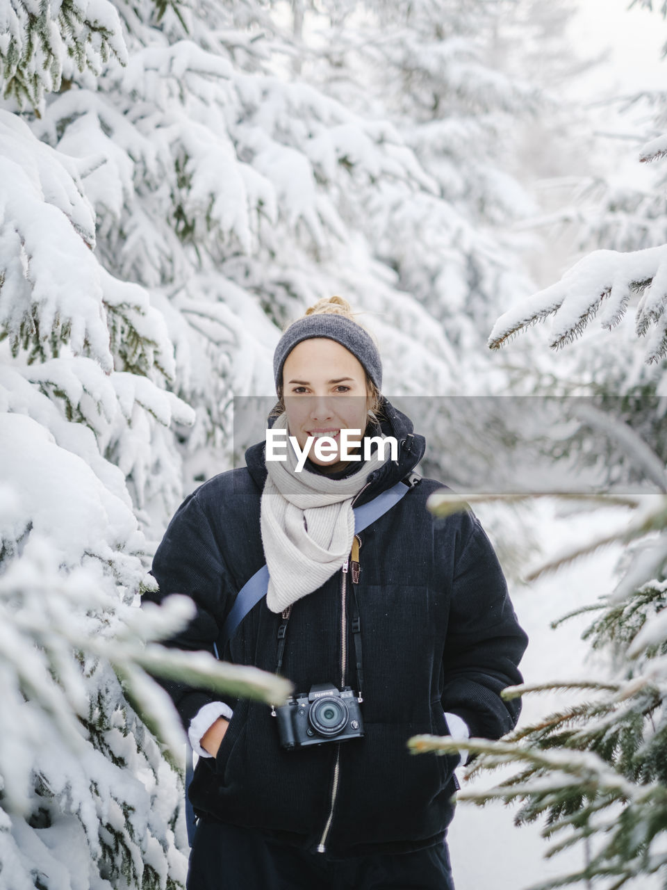 Portrait of woman with camera standing in snowy forest