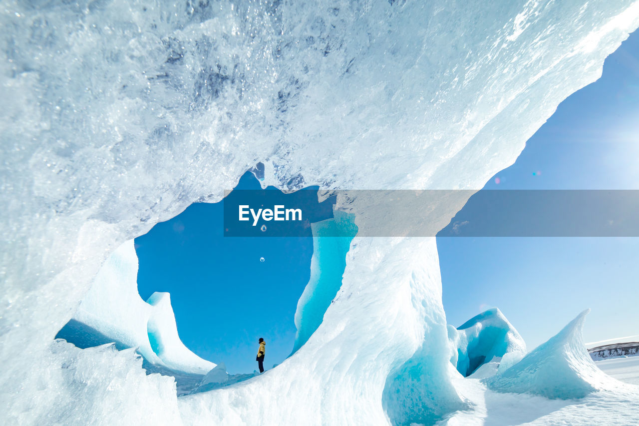 Unrecognizable traveler hiker admiring spectacular scenery of frozen seashore with ice and snow in winter in iceland