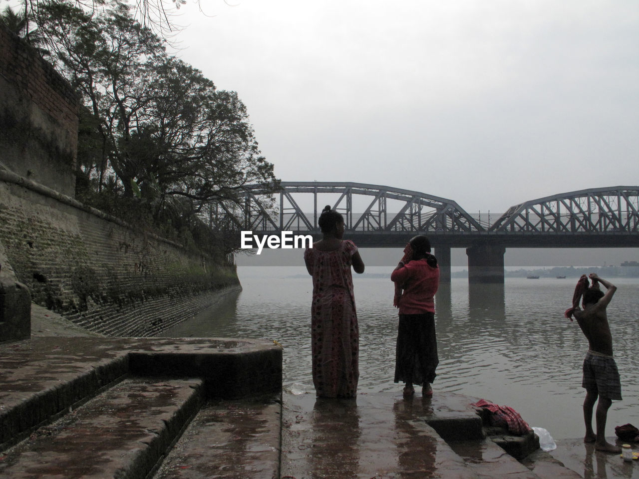 Women standing on steps by river against ganga railroad bridge