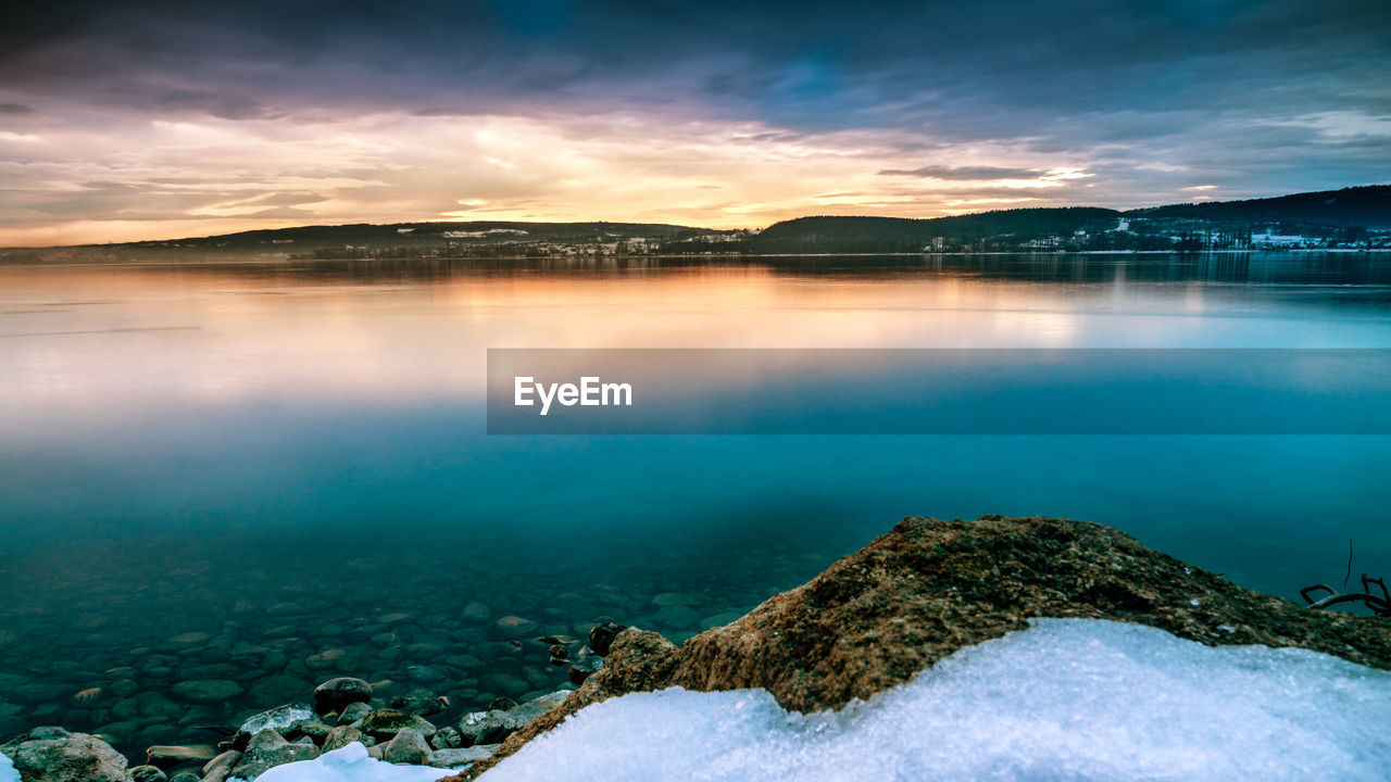 Beautiful sunrise on lake constance with stones on the lake shore and snow