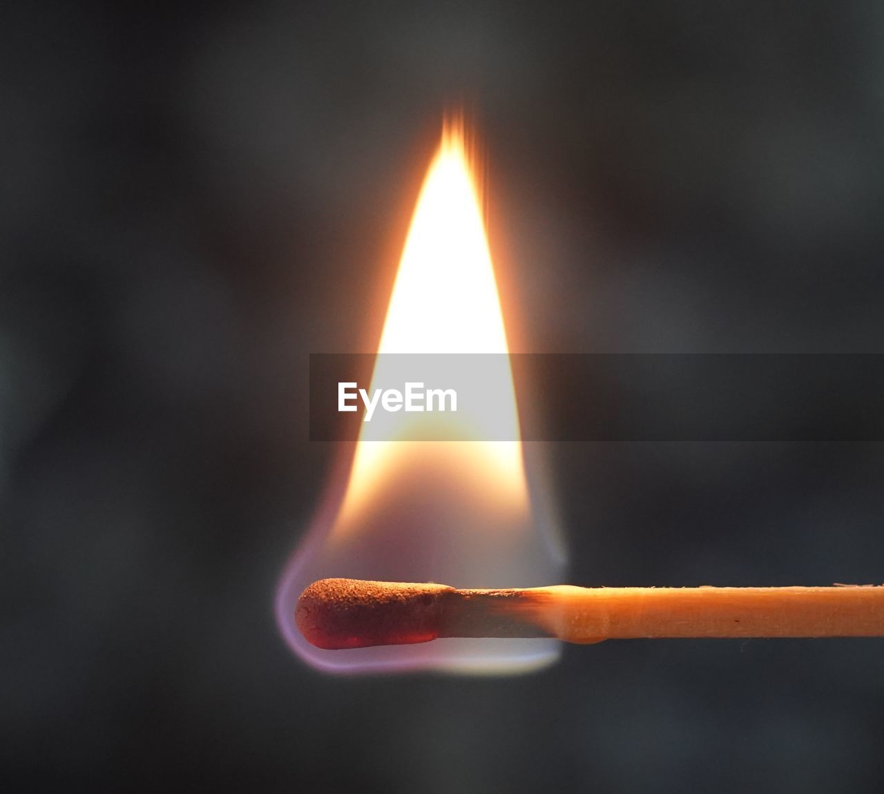 Close-up of burning matchstick against gray background