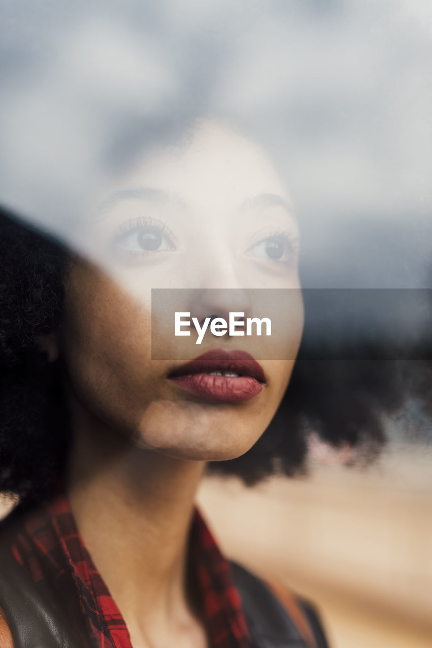 Thoughtful woman with nose pierced seen through glass