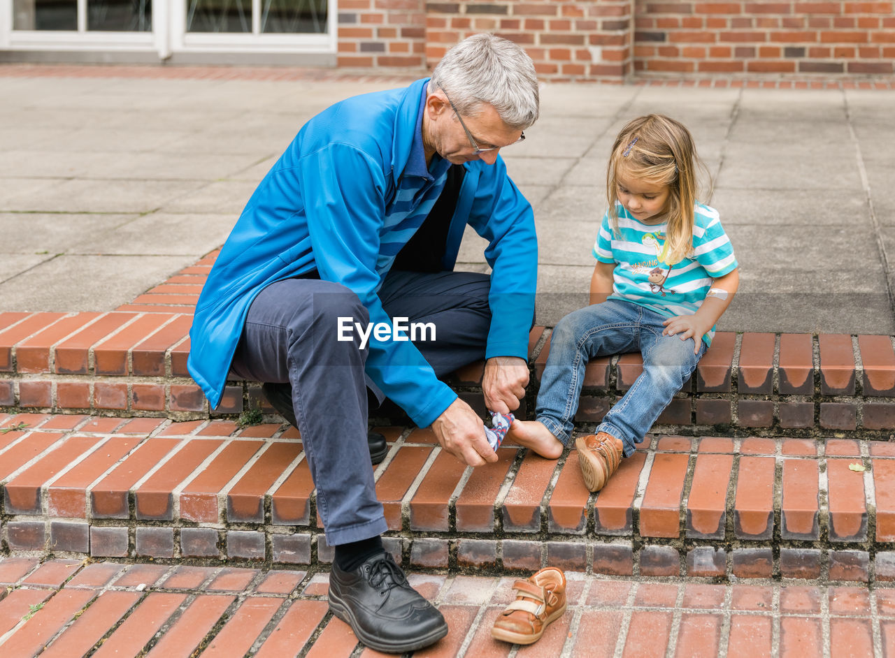 Senior man adjusting sock of granddaughter while sitting on steps