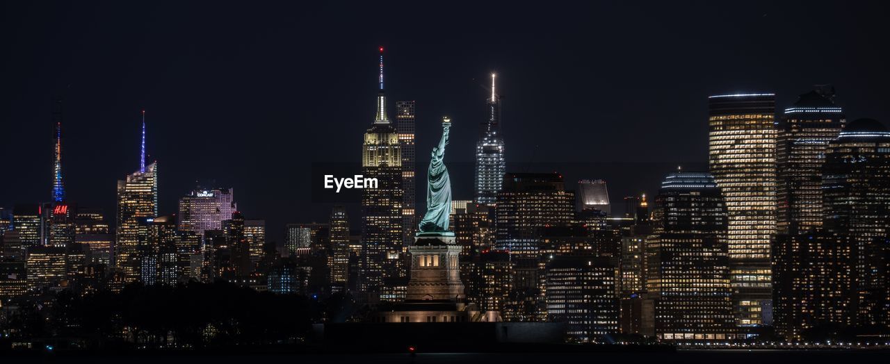 Illuminated buildings and statue of liberty in city at night