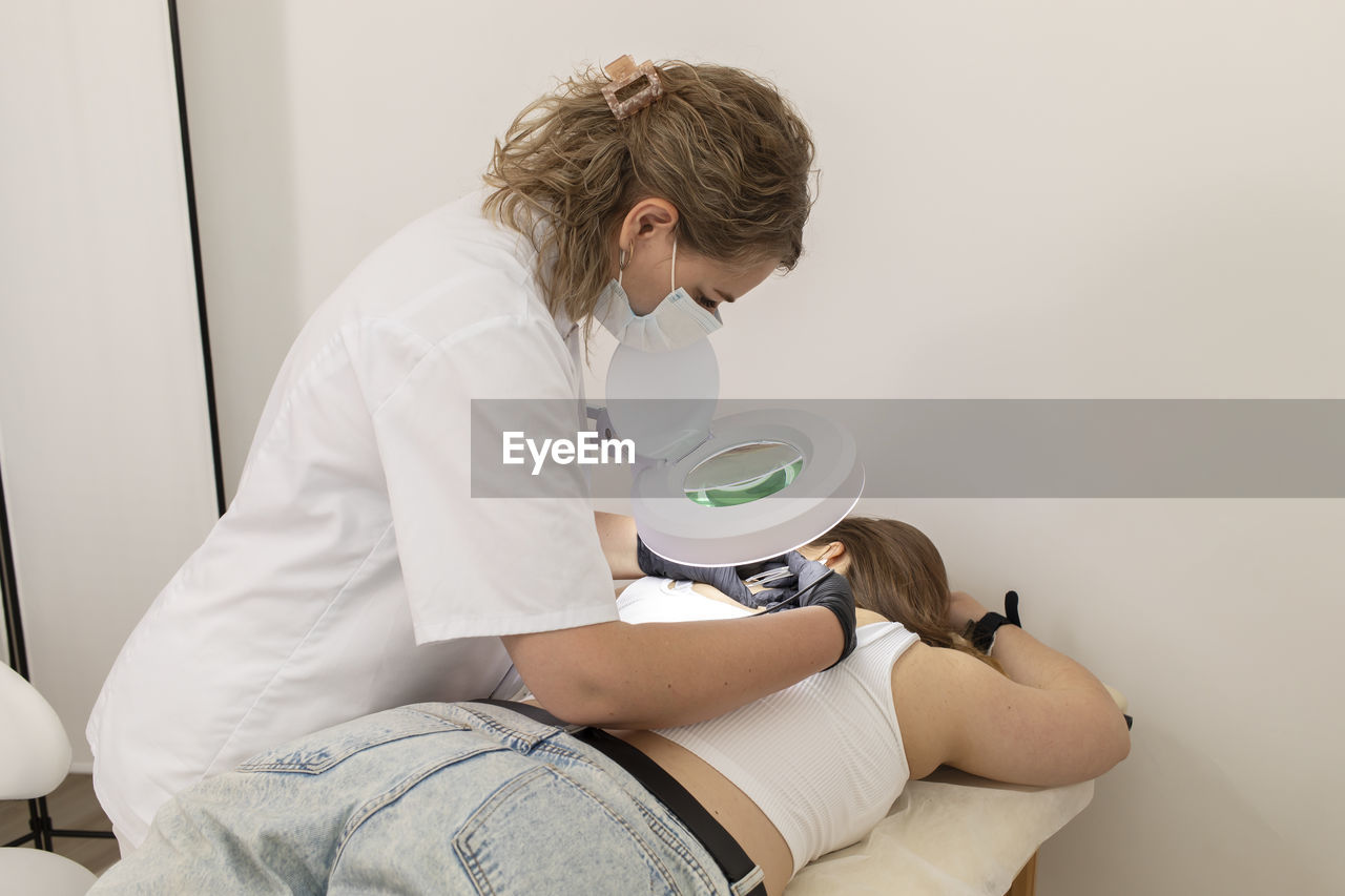 Master removes hair with electrolysis procedure on female back, electric epilation in beauty salon