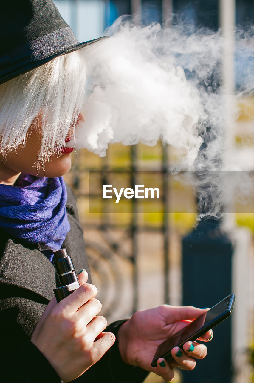 Young woman using mobile phone while smoking at park