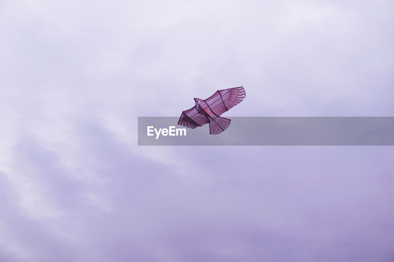 Low angle view of kite against cloudy sky