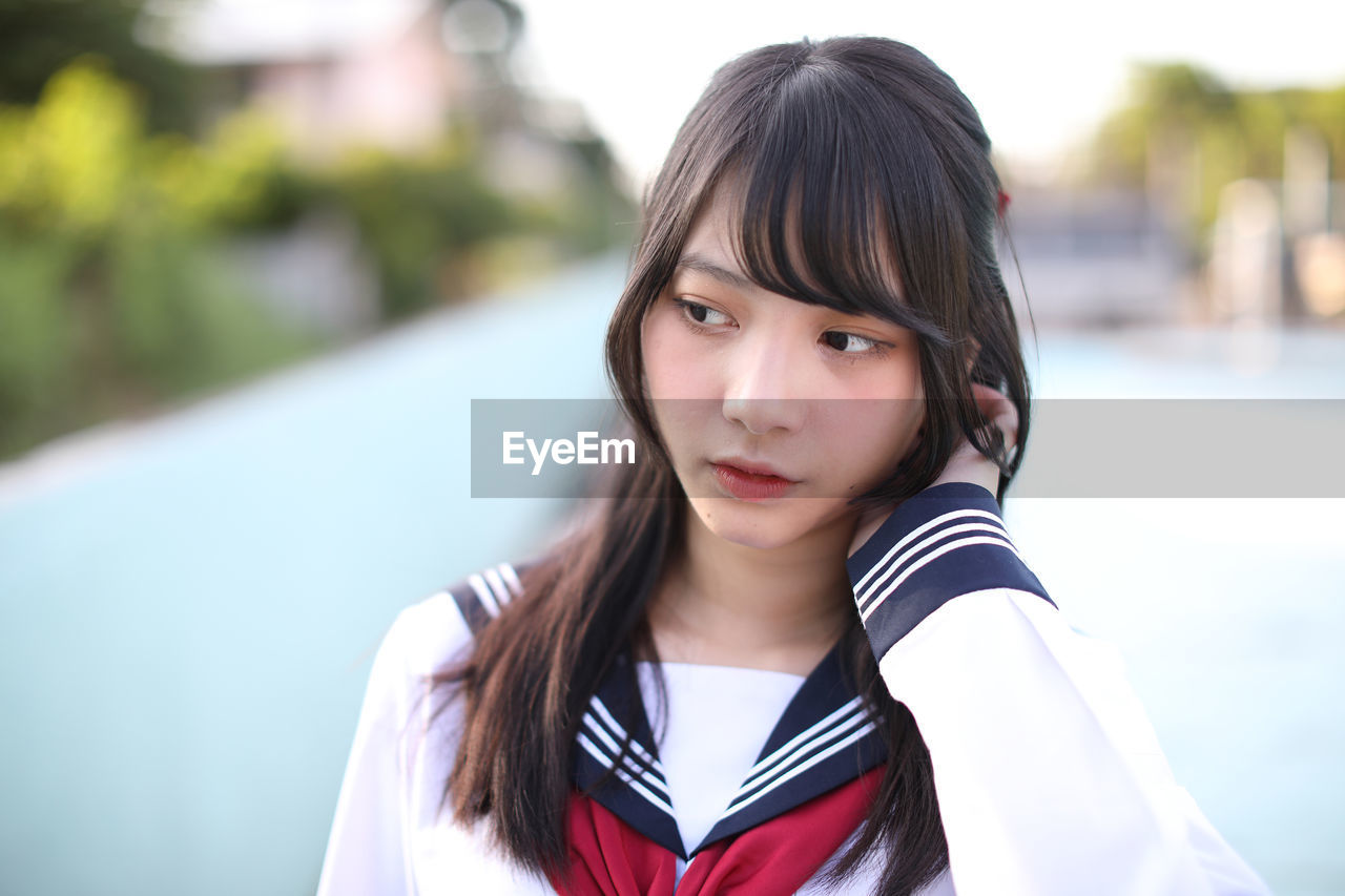 Young woman looking away while standing against blurred background