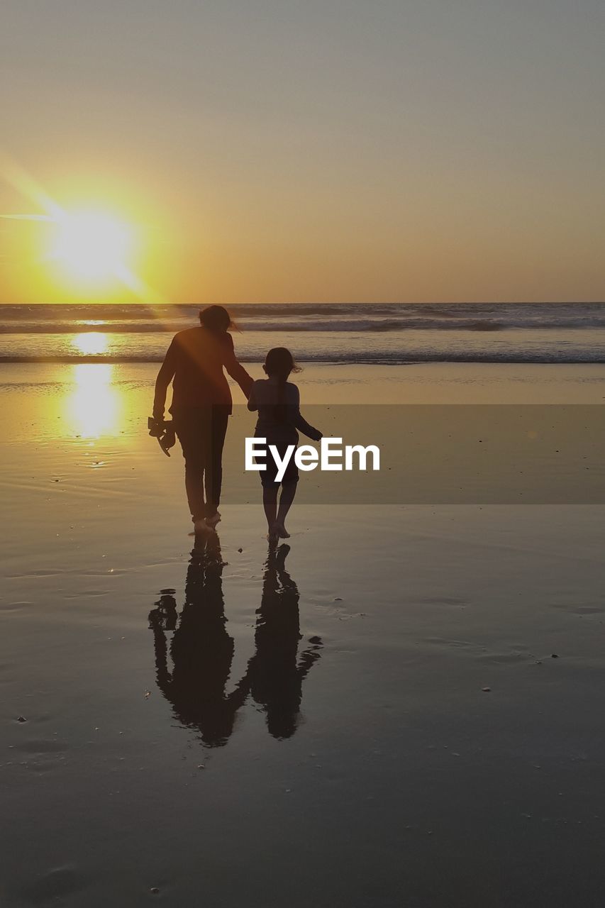 Rear view of woman with daughter walking on shore at beach