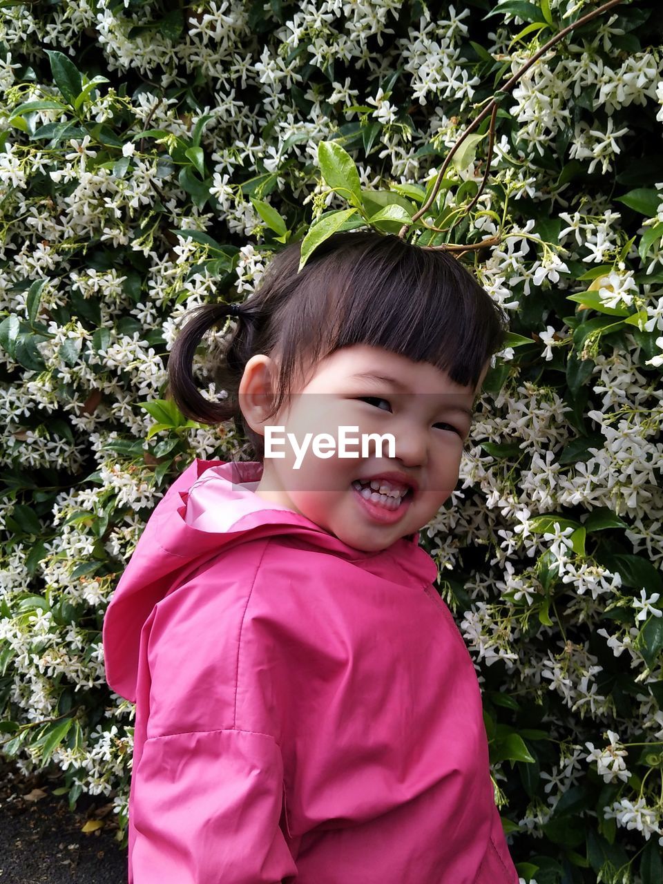 Portrait of cute girl smiling while wearing pink jacket against plants