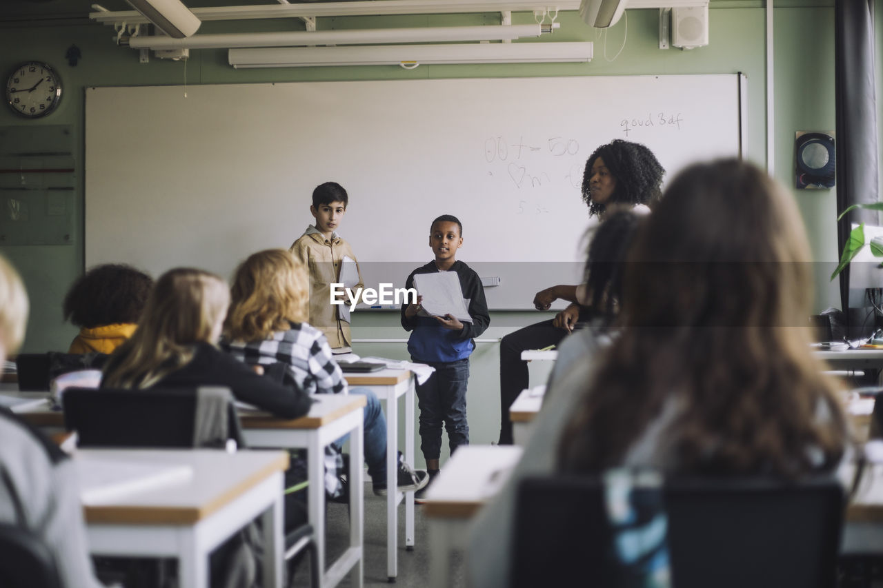 Boys holding reports while doing presentation to students in classroom