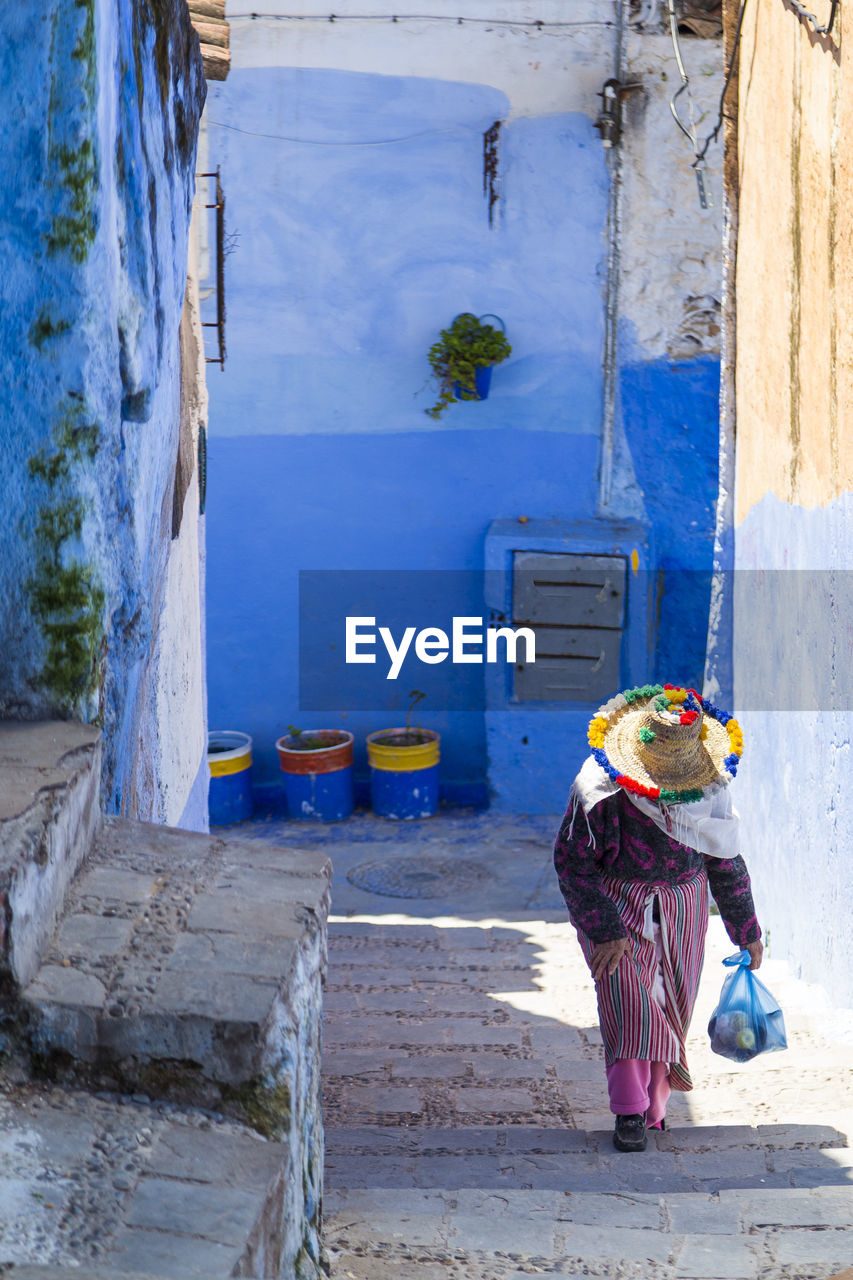 blue, wall, architecture, one person, full length, built structure, clothing, urban area, day, occupation, adult, building exterior, street, working, men, road, women, outdoors, nature, building, person, hat, rear view, wall - building feature, female, headwear, protection, lifestyles, standing, manual worker