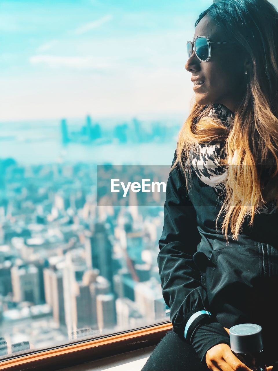 Woman looking through window against cityscape