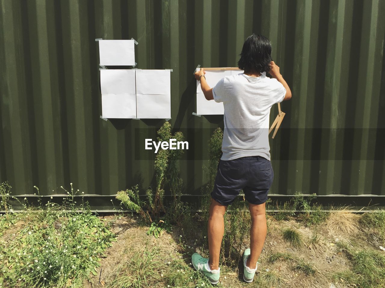 Rear view of man sticking papers on green metallic wall