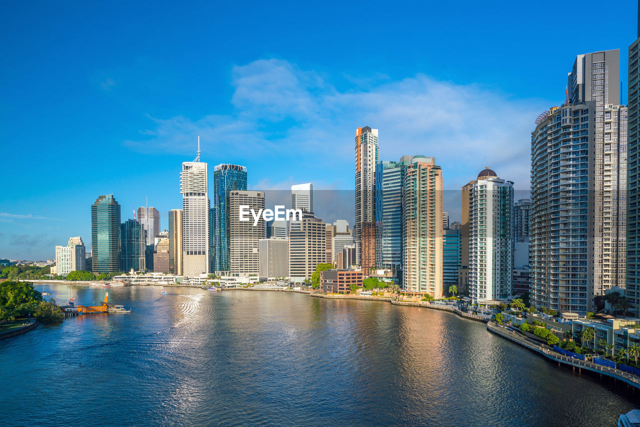 buildings by river against blue sky