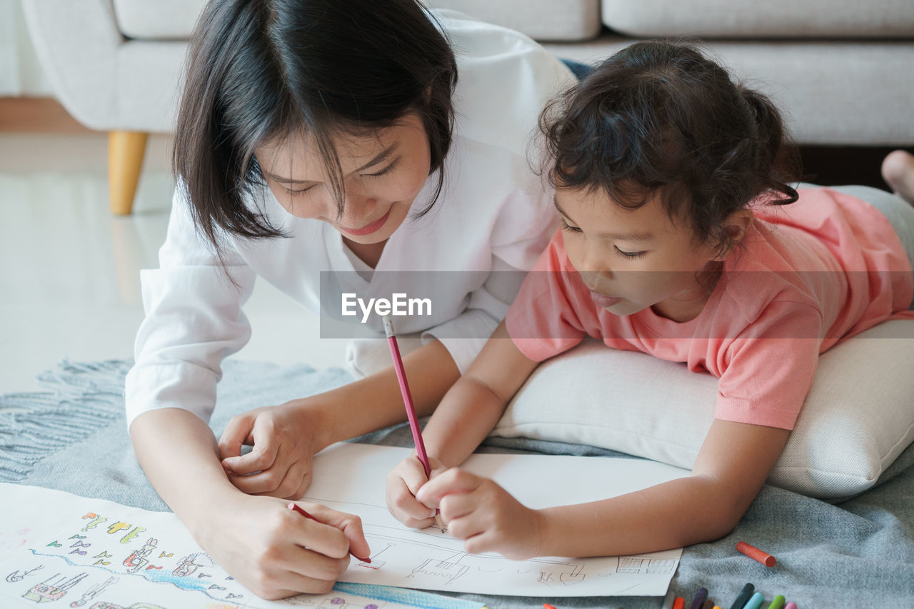 Mother and daughter drawing while lying on floor at home