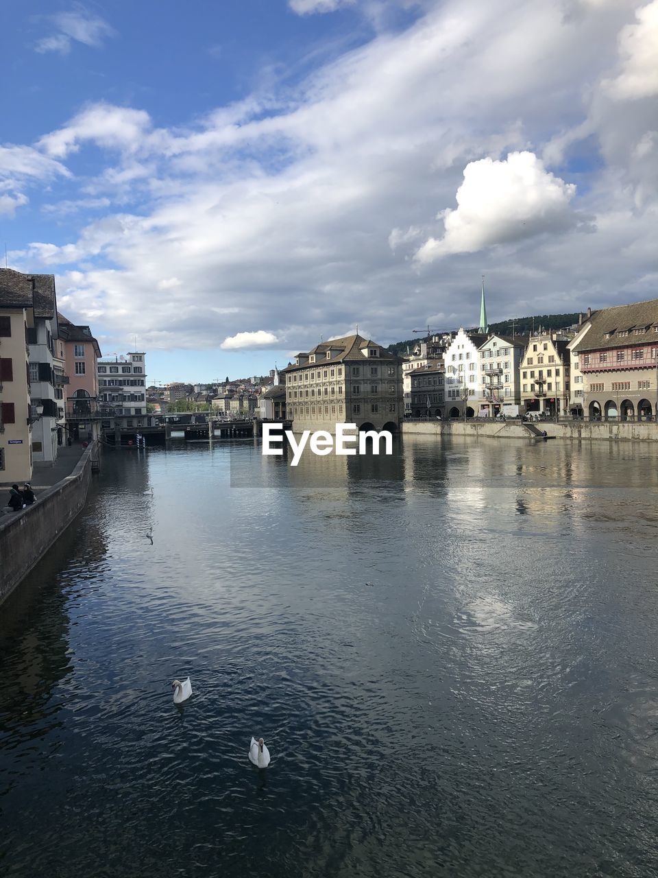 View of buildings by river against cloudy sky