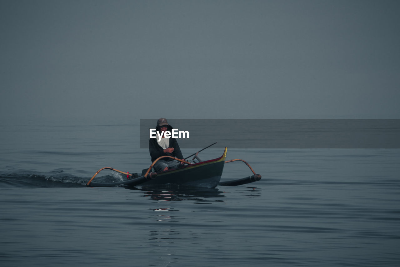 Man rowing boat in sea against sky