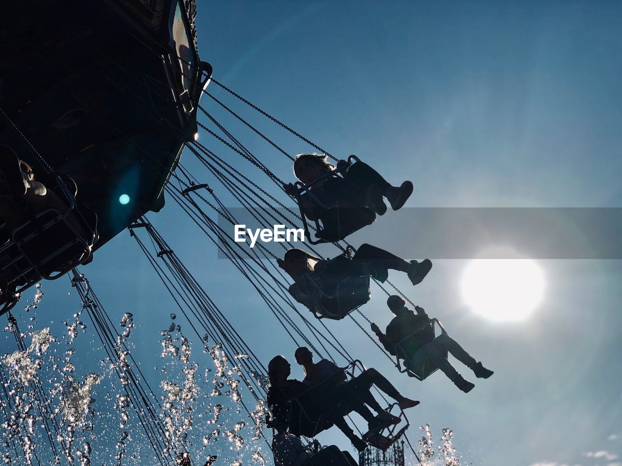 Low angle view of people enjoying chain swing ride at amusement park against sky