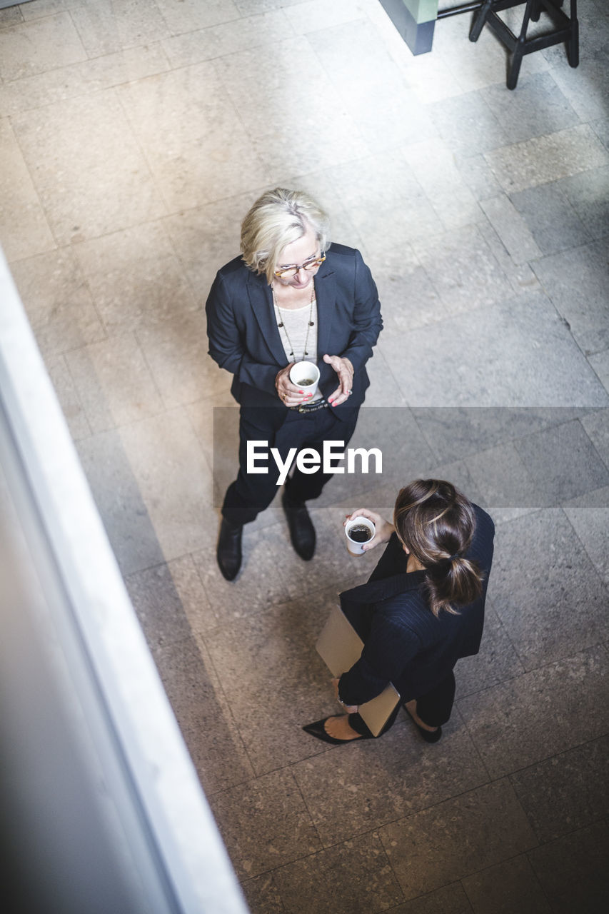 High angle view of female colleagues drinking coffee while standing in office