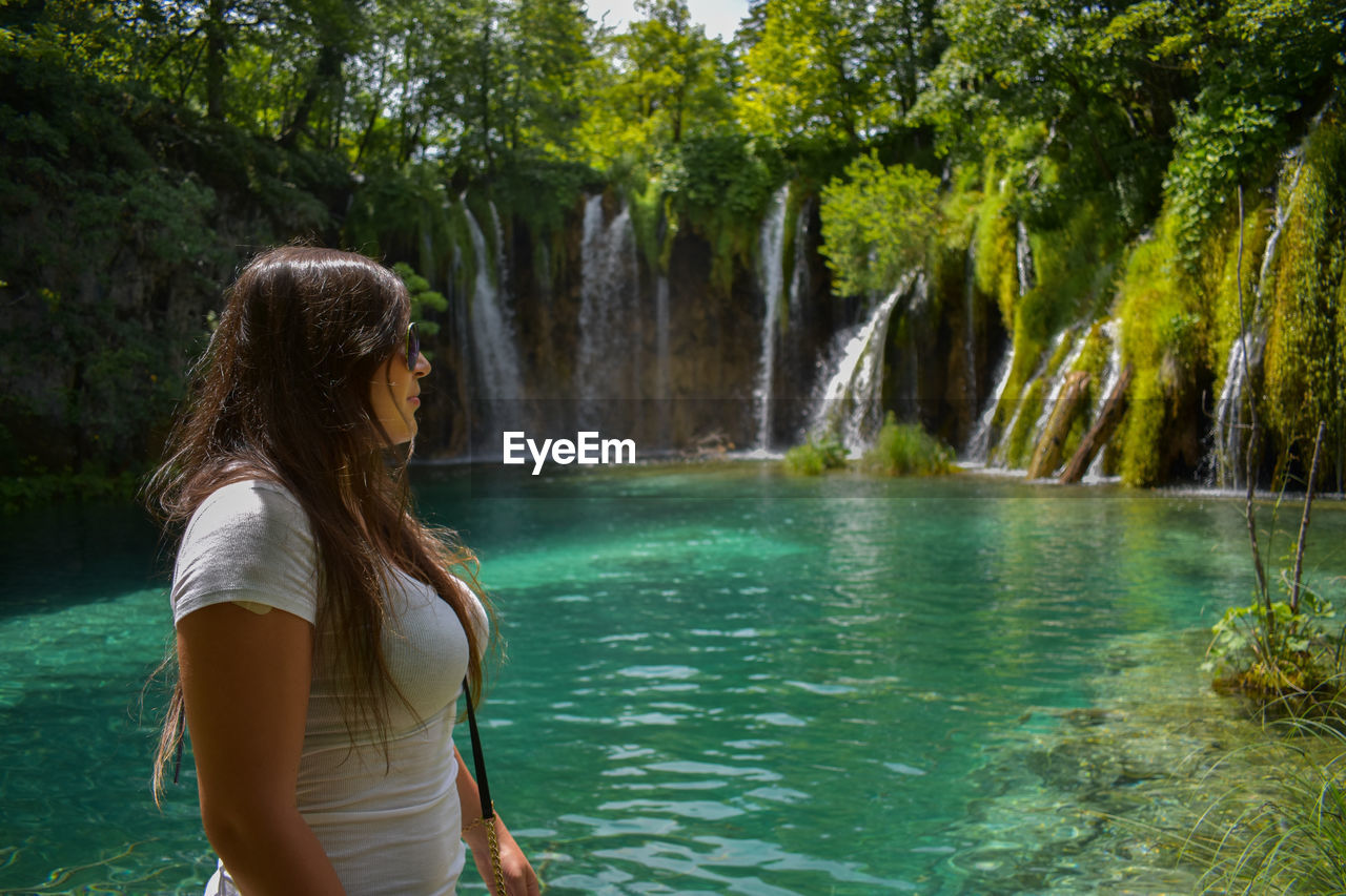 Side view of woman looking away while standing against waterfall