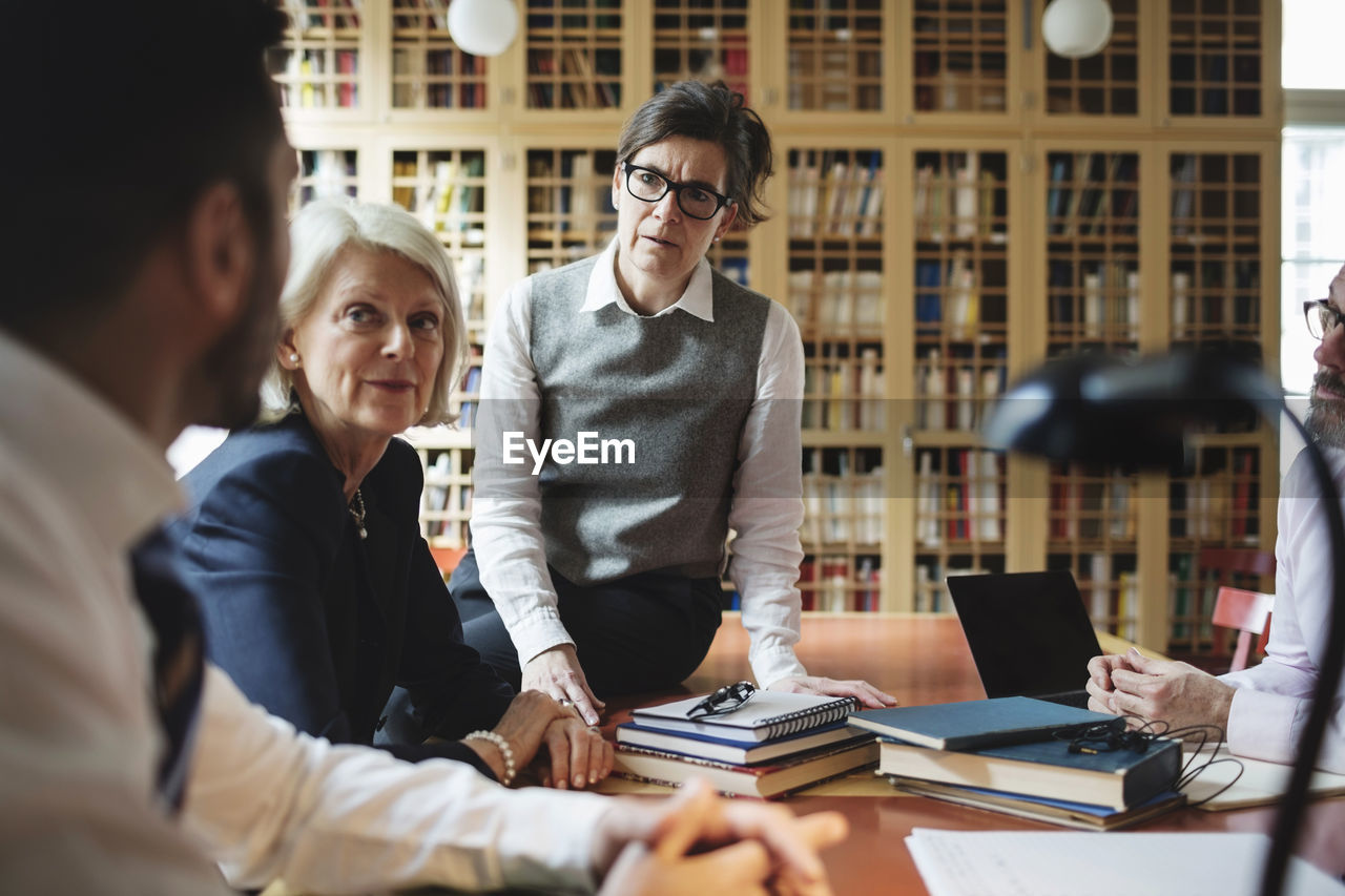 Female lawyers listening to coworker sitting at table in library