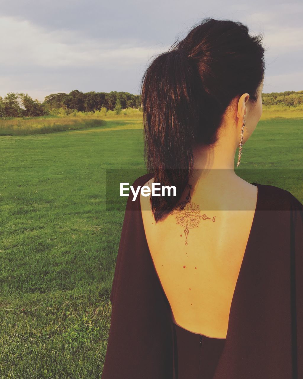 Rear view of young woman with tattoo on back at grassy field