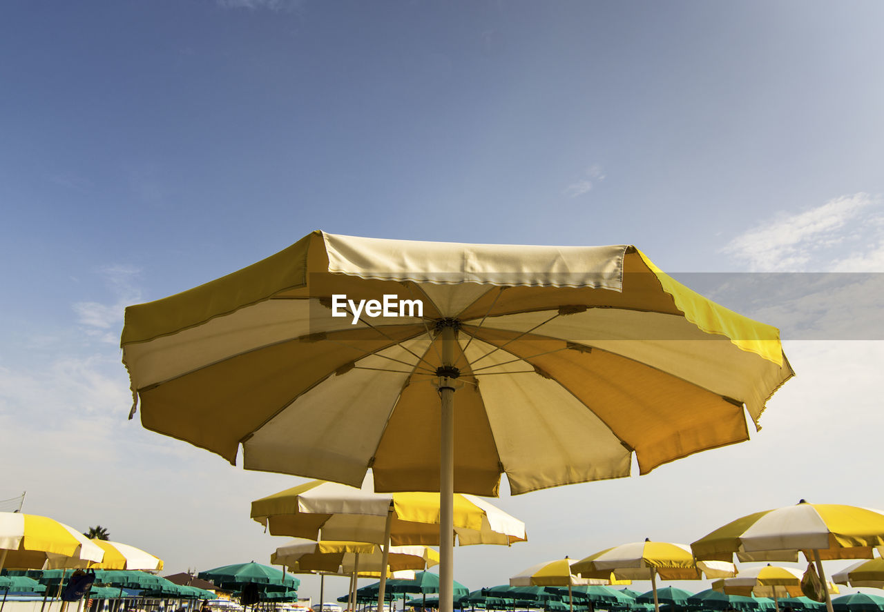 Low angle view of yellow parasols against blue sky during sunny day