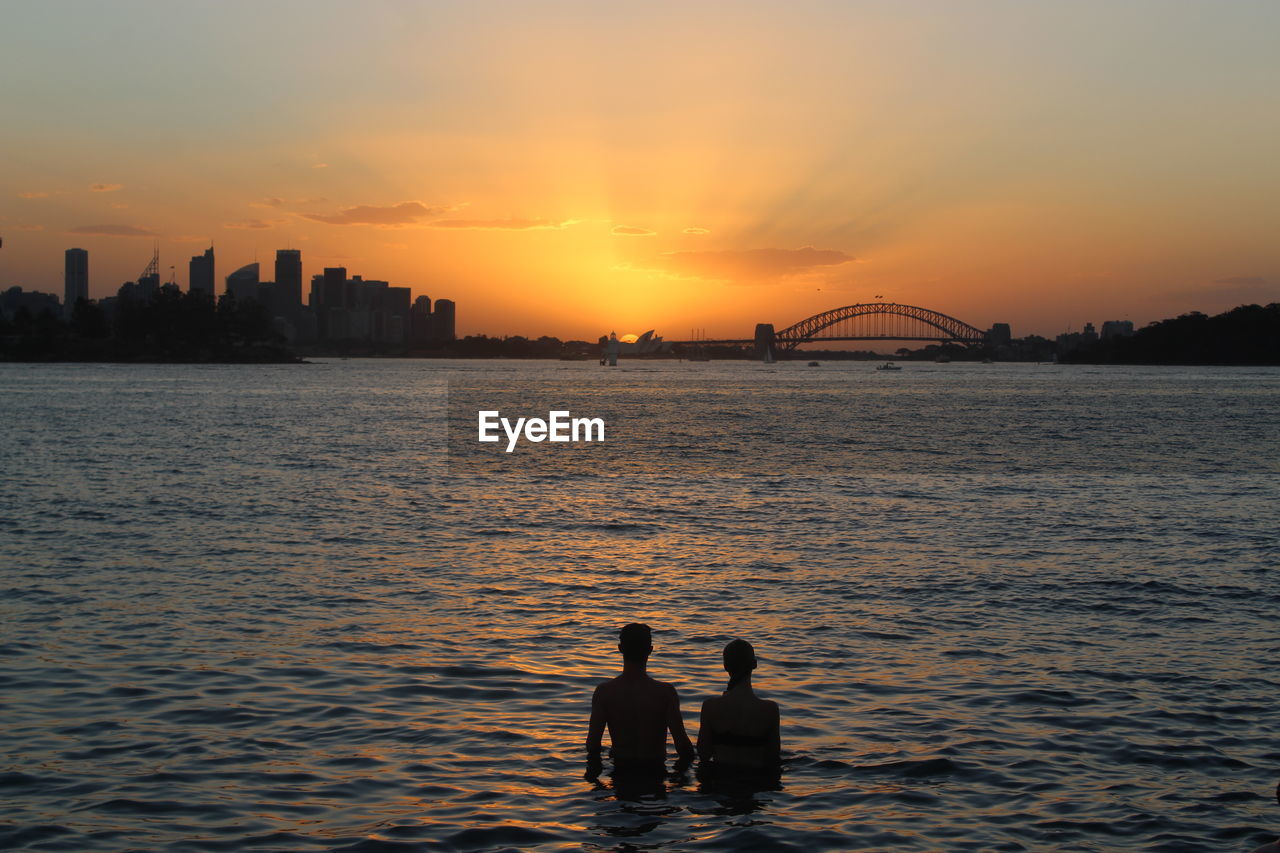 Silhouette couple in sea against sky during sunset